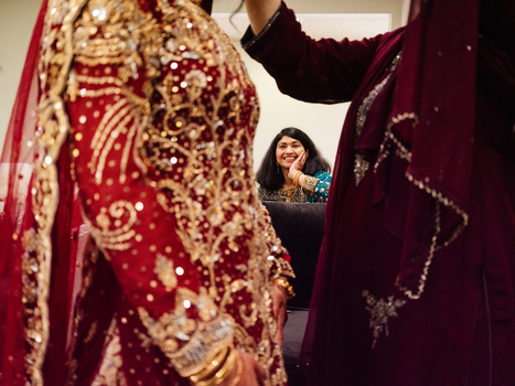 Woman smiling while examining ornate red and maroon embroidered garments with gold beadwork and detailed embellishments.