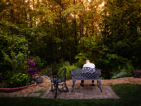 Person in white shirt seated at ornate black table in lush woodland garden at golden hour.