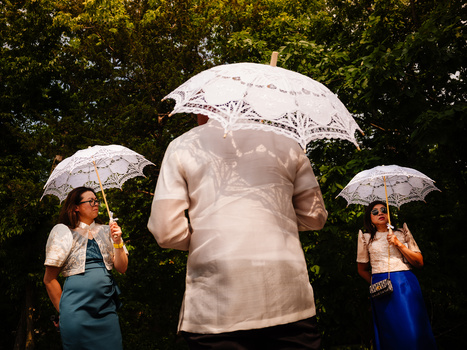 Three people holding decorative lace umbrellas pose outdoors against green foliage.