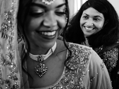 Two women in ornate traditional attire smiling together in a black and white portrait.