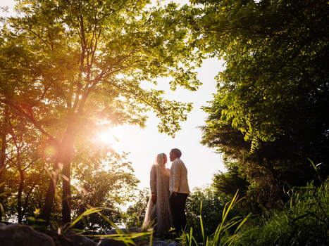 Couple standing together in a park at golden hour with trees backlit by sunset.