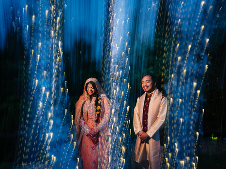 Two people standing between illuminated blue vertical light installations at night.