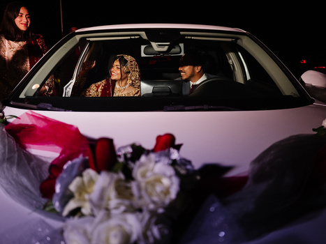 Bride and groom in a white car at night with wedding flowers in the foreground.