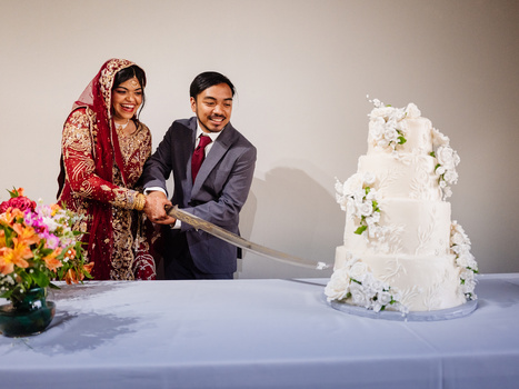 Bride and groom cutting a white tiered wedding cake decorated with flowers.