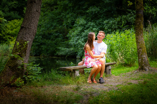 Adult and child sitting together on a wooden bench in a shaded forest setting.