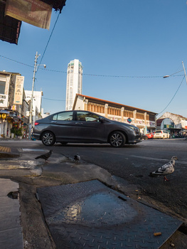 Dark sedan driving through an urban street with puddles reflecting sky and buildings.