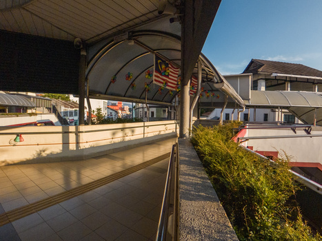 Covered walkway with strong directional shadows cast by the pergola structure onto the pavement.