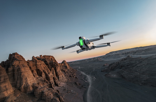 Drone with bright green accents flying over rocky canyon terrain at sunset.