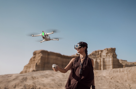 Operator in VR headset controlling a drone in flight over desert rock formations.