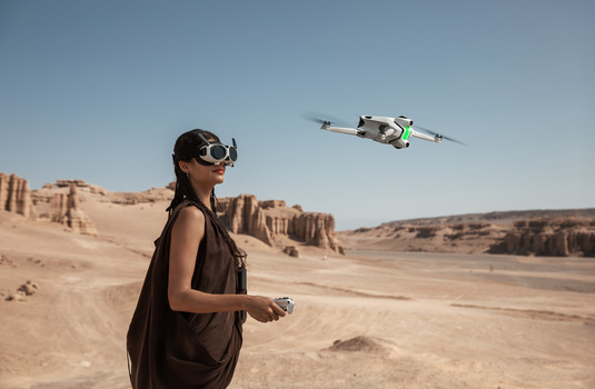 Drone pilot operating a quadcopter in a desert landscape with rocky formations in the background.