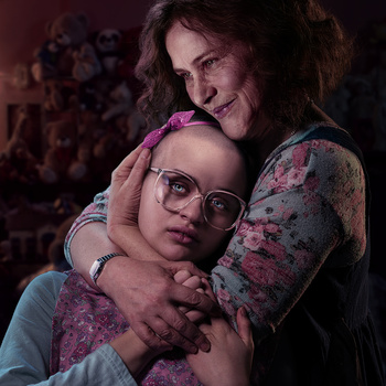 Two people embracing in warm, moody lighting with burgundy and purple tones.