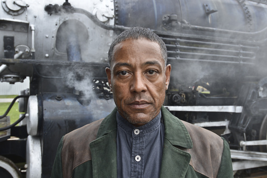 Man in olive jacket and denim shirt facing camera in front of a steam locomotive.