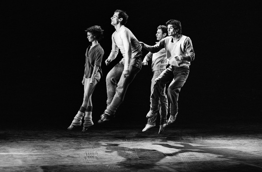 Five musicians jumping in unison against a black background during a performance.
