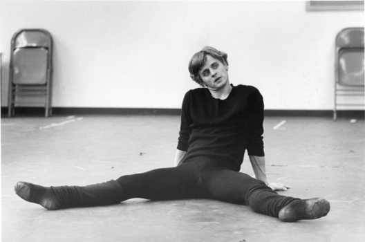 Person in black clothing performing a wide leg split on a concrete floor in an empty studio space.