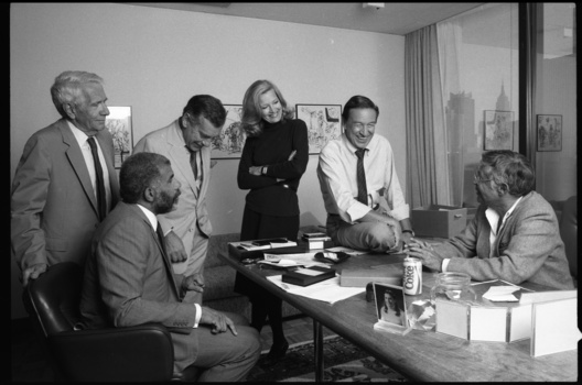 Six people in business attire gathered around a conference table in an office setting.
