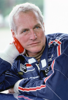 Portrait of an older man with white hair wearing a dark blue racing jacket with red and white stripes.