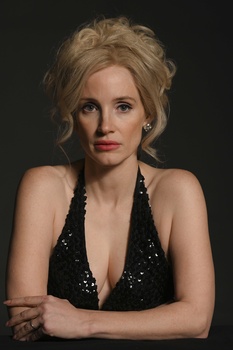 Woman with blonde upswept hair wearing black sequined halter top against dark background.