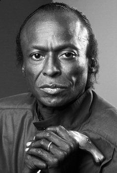 Black and white portrait of a man with clasped hands against his chest, direct gaze toward camera.