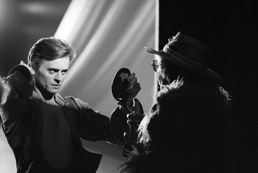 Man in dark clothing holding a falcon in black and white dramatic lighting.