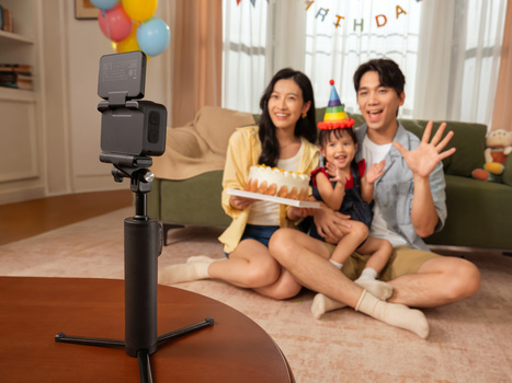 Family of three recording a birthday celebration video on a smartphone mounted on a tripod.