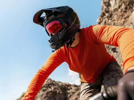 Mountain biker in red and yellow gear wearing a black helmet with red-tinted goggles on a rocky trail.