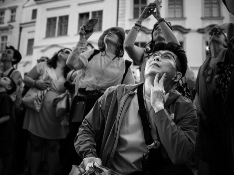 Man gazing upward with hand to face amid crowded urban gathering, captured in black and white.