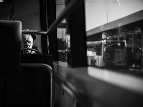 Elderly man visible through bus window, shot in black and white with shallow depth of field.