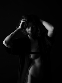 Woman in dramatic studio lighting poses with hands near head against dark background.