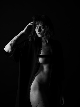 Woman in dramatic black and white portrait with hand raised to head against dark background.