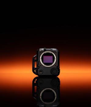 Mirrorless camera body with exposed sensor displayed against warm orange and black gradient background.
