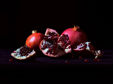 Pomegranates with split skin revealing deep red arils against a dark background.
