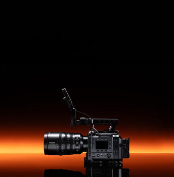 Professional cinema camera with attached lens and microphone against warm orange backdrop.