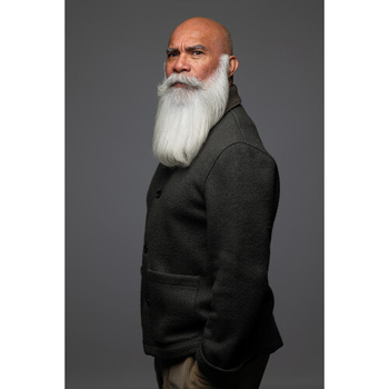 Older man with long white beard wearing dark blazer against gray background.