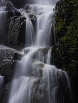 Cascading waterfall flowing over moss-covered rocks in multiple tiers.