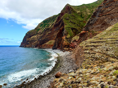 Steep coastal cliffs with lush green vegetation dropping to a rocky beach and turquoise ocean.