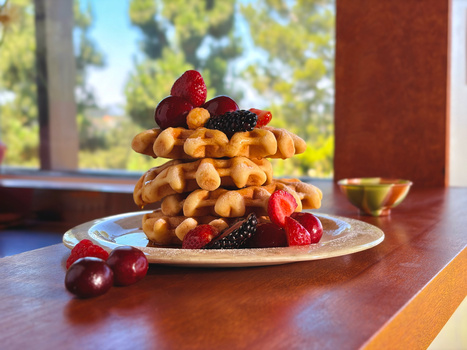 Tower of golden pastry puffs topped with fresh berries on a wooden plate.