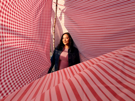 Woman posed within a geometric tunnel of pink and white striped and checkered patterns.