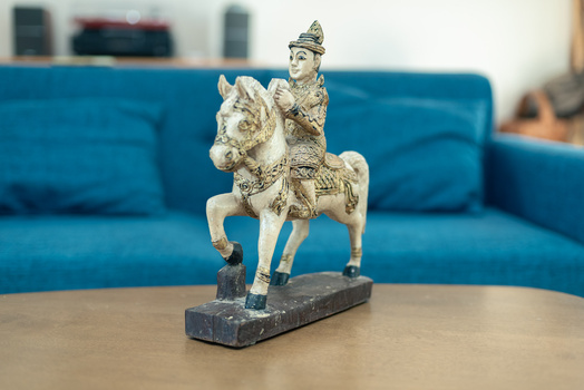 Ornamental figurine of a robed figure riding a decorated horse, displayed on a wooden table.