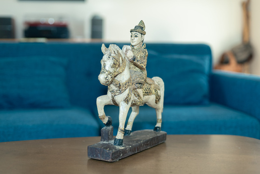 Ornamental statue of a figure on horseback mounted on a dark stone base, displayed on a wooden table.
