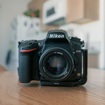 Nikon D750 DSLR camera with AF Nikkor lens on wooden desk.
