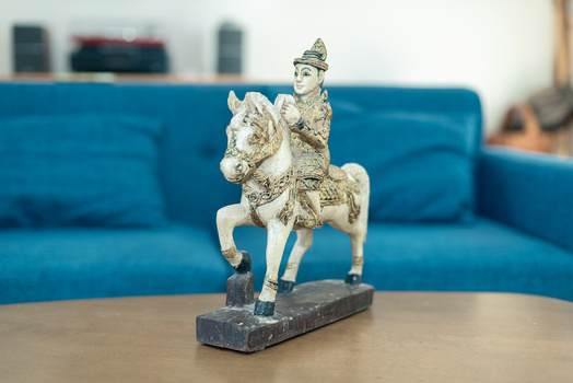 Decorative figurine of a figure on horseback, rendered in cream and green tones, displayed on a wooden surface.