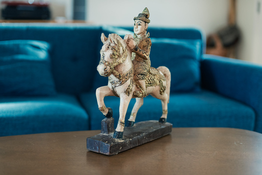 Ornamental figurine of a rider on horseback mounted on a dark stone base, displayed on a wooden table.