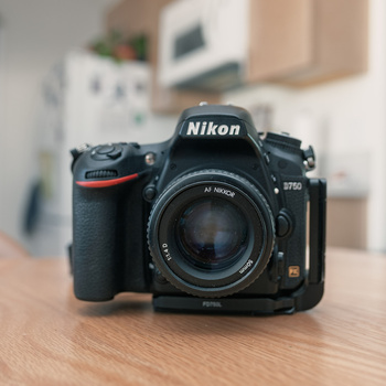 Nikon D780 DSLR camera with standard lens on wooden surface, blurred interior background.