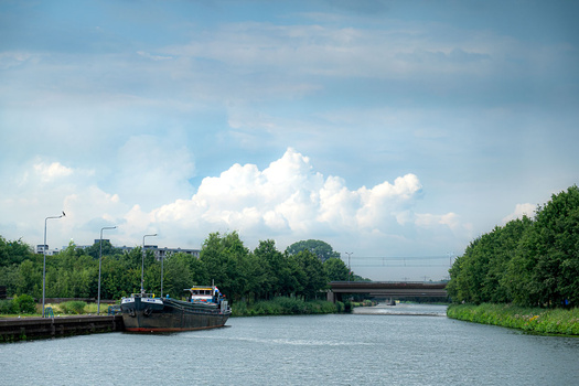 Industrial barge moored alongside a canal under cumulus clouds and blue sky.
