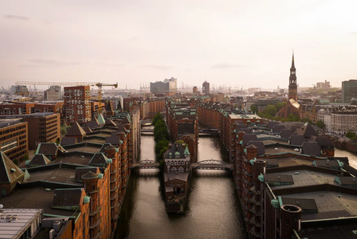 Elevated view of parallel waterways cutting through dense urban residential architecture with a church spire visible on the horizon.