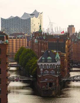 Red brick building surrounded by water channels with modern skyscrapers in the background during golden hour.