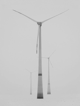 Wind turbines photographed from below against an overcast sky, showing their tall towers and blade structures.