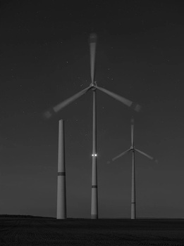 Three wind turbines of varying heights silhouetted against a dark sky at dusk or night.