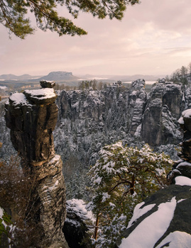 Snow-dusted rock formations and evergreen forest stretching across a vast canyon valley.