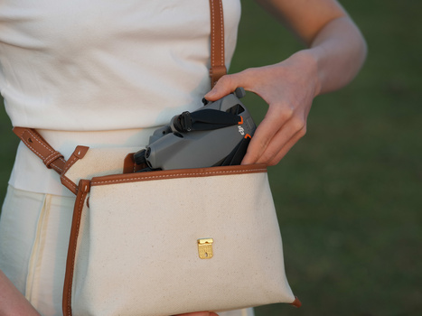 Person holding a compact camera while wearing a cream-colored crossbody bag with brown leather straps.